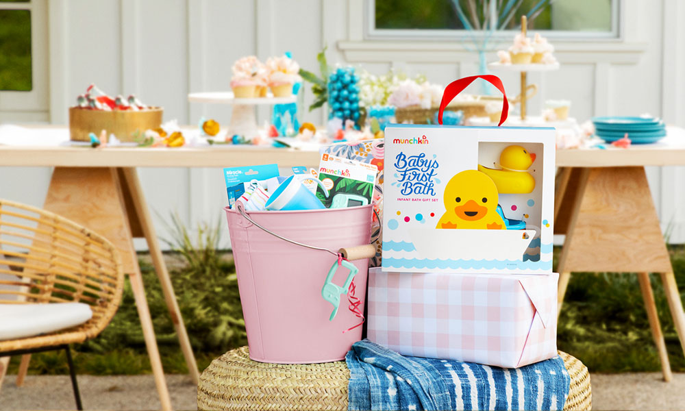 A selection of munchkin products sit in front of a baby shower table holding cupcakes and other party food