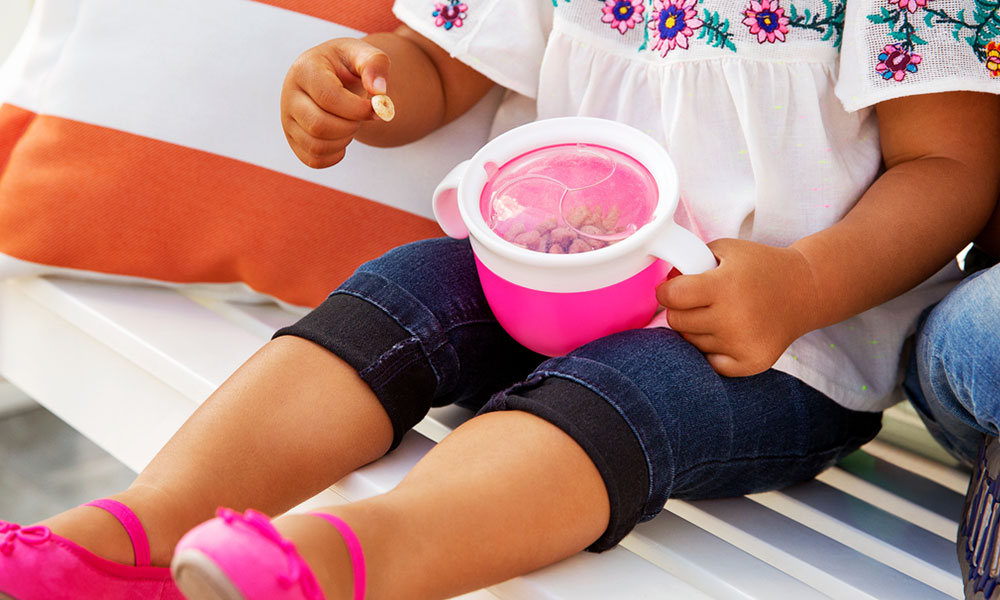 A child sits with a munchkin snack catcher, eating snacks