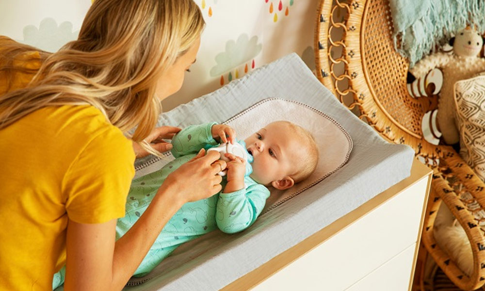 A mum leans over to play with her baby on a nappy changing mat