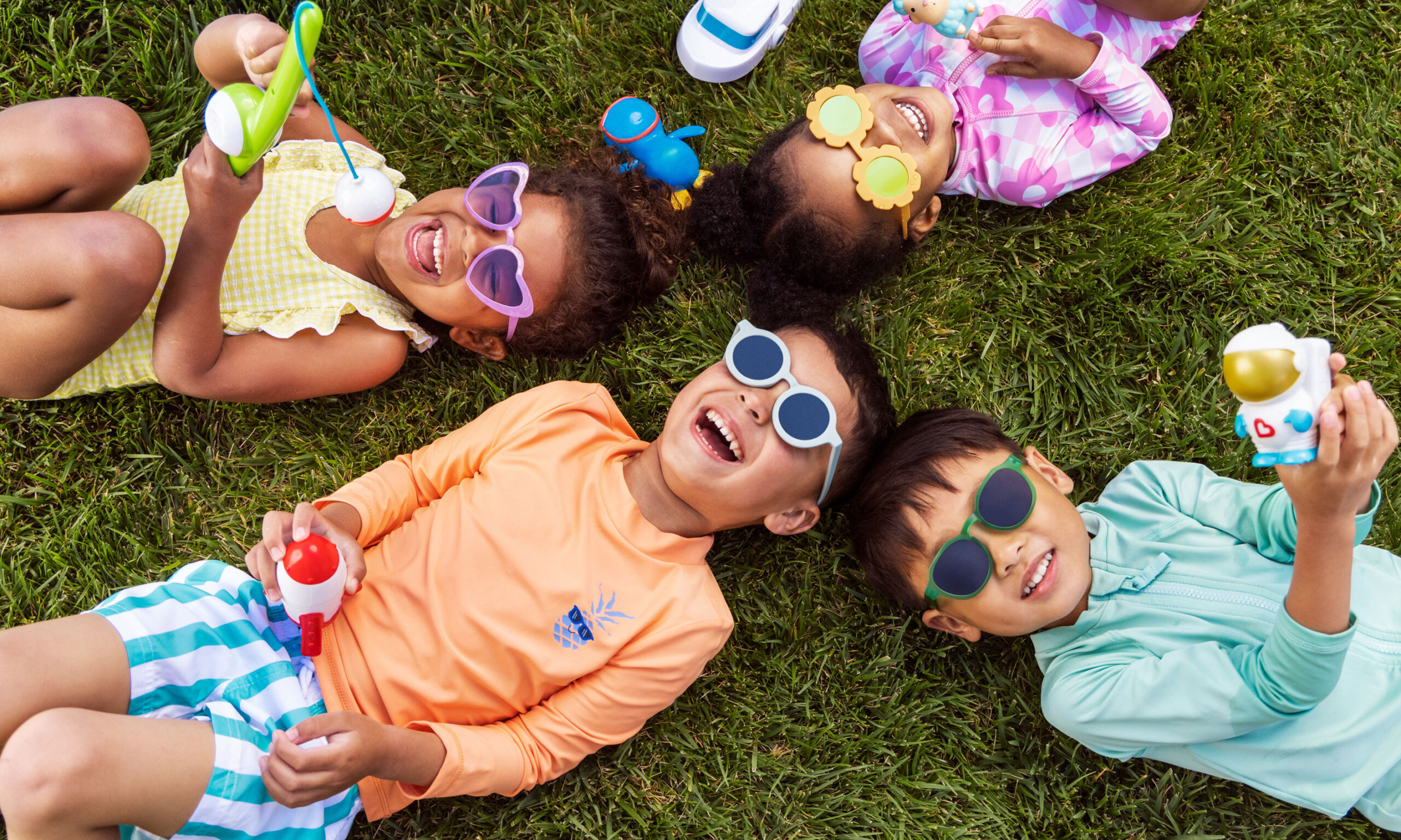 Four children laying on their backs on the grass, playing with bath toys