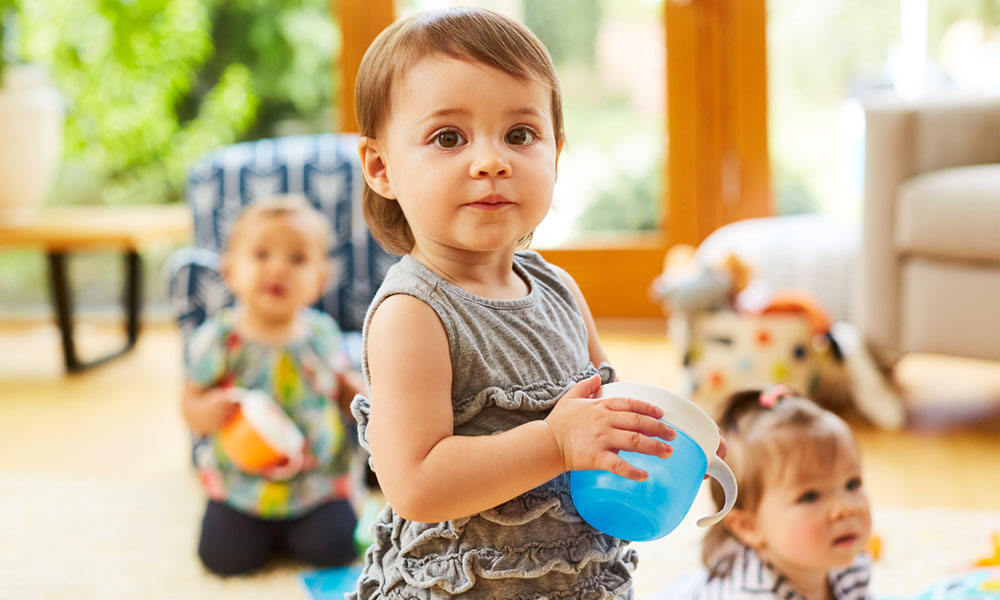 Toddler playing together in living room, with little girl holding a Munchkin Snack Catcher