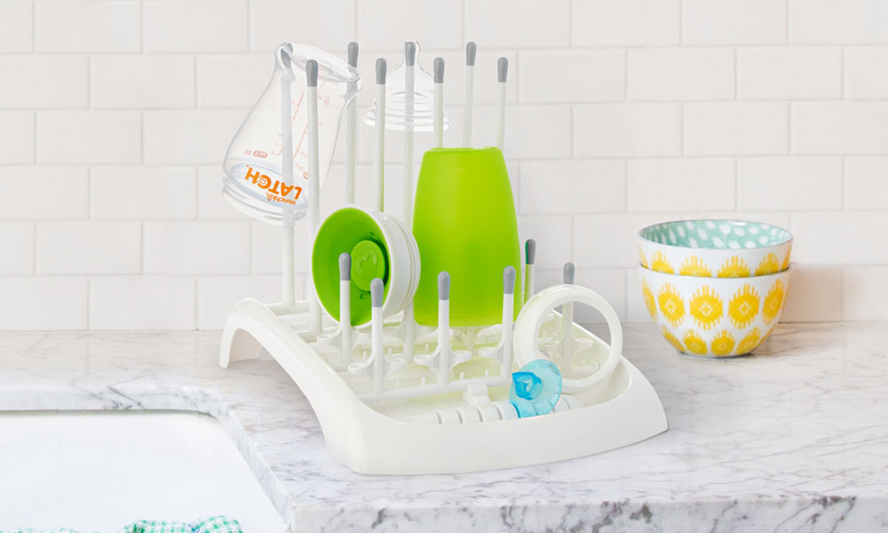 A Munchkin baby bottle drying rack sits on a kitchen worktop next to a sink