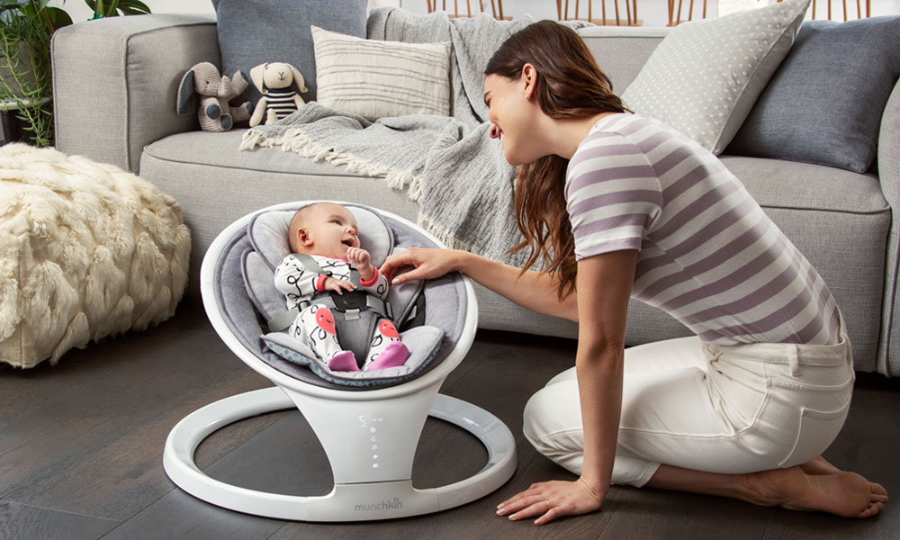 A baby sits smiling in a Munchkin baby bouncer while her mum talks to her