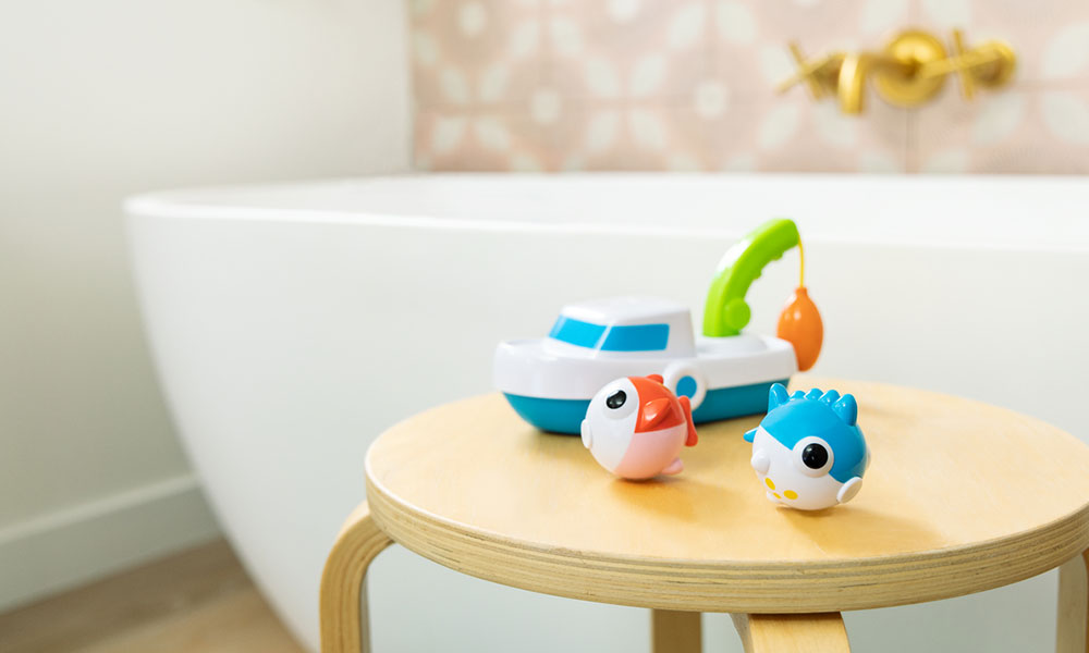 Some colourful Munchkin bath toys sit on a stool next to a bath