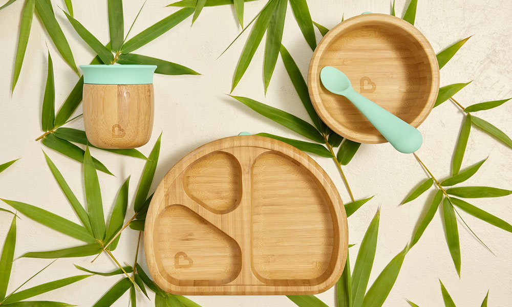 A Munchkin bamboo and silicone open cup, suction bowl and divider suction plate on a background of bamboo leaves.