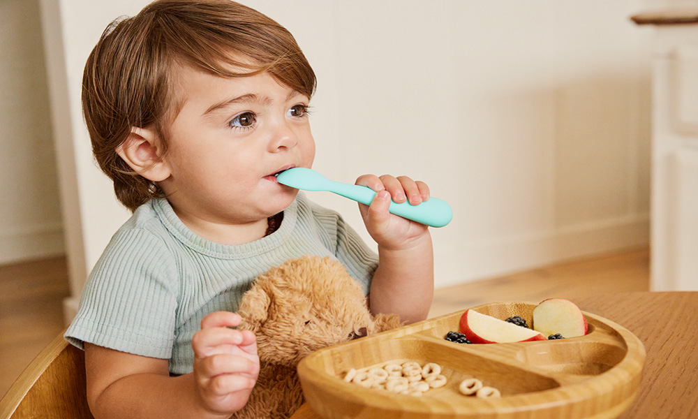 Boy eating with a spoon in his mouth.